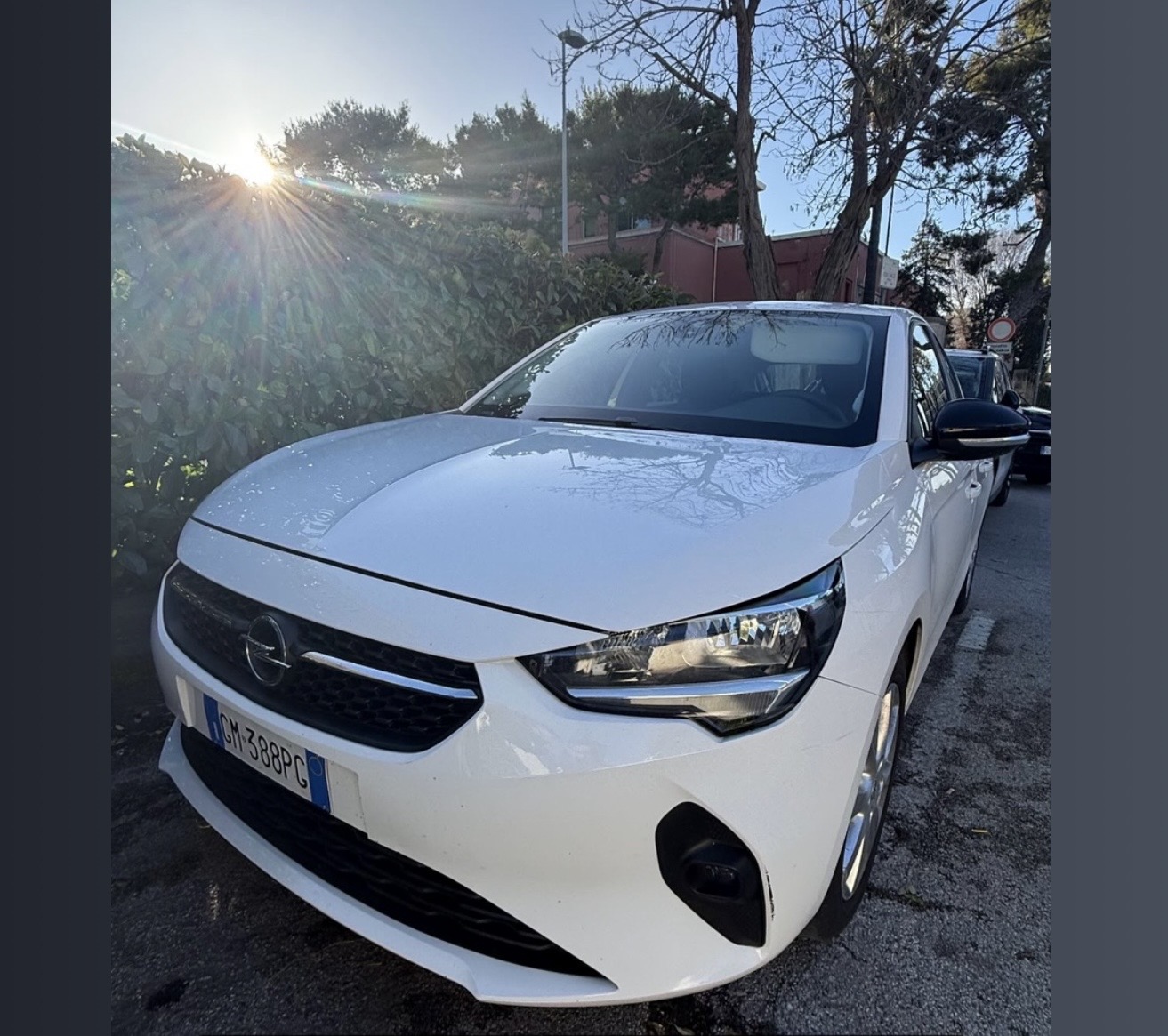 Opel Corsa bianca targata GM388PG parcheggiata accanto a una siepe in controluce, flotta DS Rentcar
